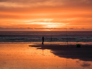 Fisherman and a Glorious Sunset at Newgale. A lone fisherman using two fishing rods looking at  a stunning sunset at Newgale in Pembrokeshire, Wales