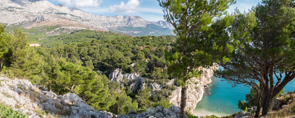 Calm blue sea with pine tree forest and mountain above