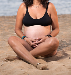 Mujer embarazada en bikini, sentada en la playa.