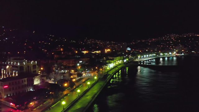 Aerial view of night Yalta city embankment with many buildings and lights reflected in sea water, drone shot