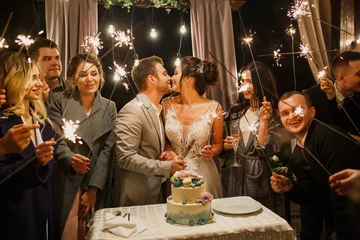 junge schöne hochzeitspaare schneiden hochzeitstorte mit freunden und haben spaß mit bengalischen lichtern © Alexander
