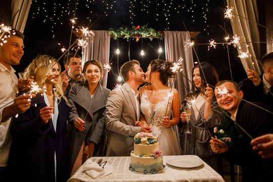 young beautiful wedding couple cut wedding cake with friends and have fun with bengal lights