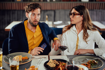 Multiethnic friends sitting at restaurant, drinking alcohol, chatting and having burgers for dinner.