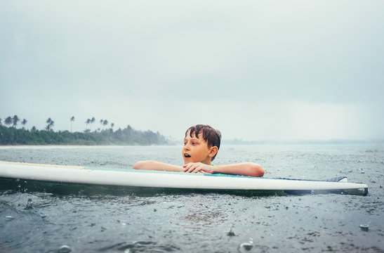 Boy learning to surf under the tropical rain. Surf school education concept image.