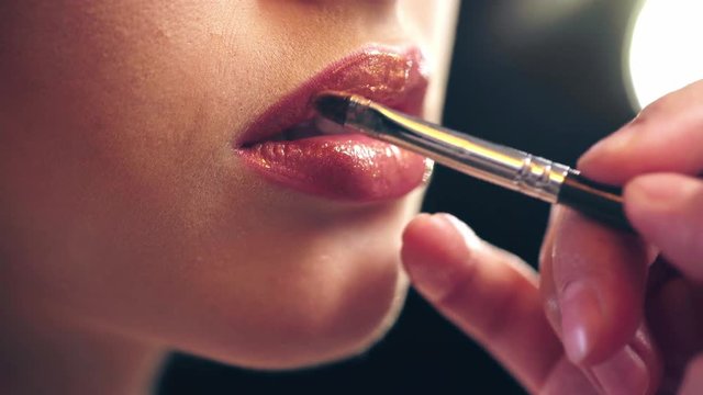 cropped view of makeup artist applying lip gloss on model lips 
