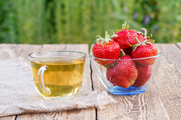 Glass cup of green tea and red ripe strawberries in glass bowl.