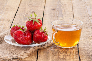 Glass cup of tea and red ripe strawberries in glass bowl.