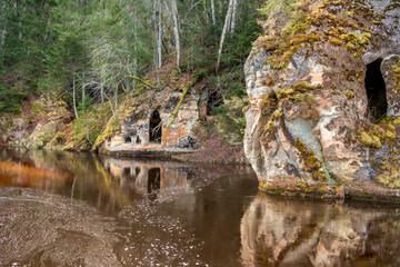 Fototapeta na wymiar Mystical Anfabrika sandstone rock with ancient chambers and caves reflecting in the river water, Ligatne, Latvia