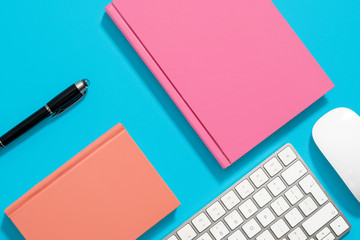Orange and pink hardcover notebooks lying flat on a pastel blue background with an iMac keyboard...