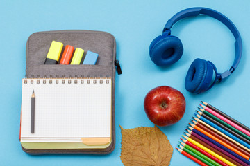 Color pencils, apple, headphones, open exercise book on bag-pencil case with color felt pens and...