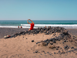 Surfer girl resting on a dry stone wall, Famara beach and surfers. Lanzarote, Canary Islands, Spain. Africa