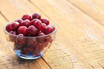 Ripe cherries in glass bowl on old wooden boards.