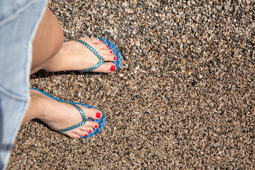 Women's feet in the blue flip flops on a pebble beach, copy space.