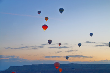 Flight of balloons over a mountain valley at sunrise.