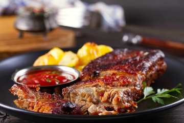 Grilled pork spare ribs with fries on black plate. Roasted sliced barbecue ribs