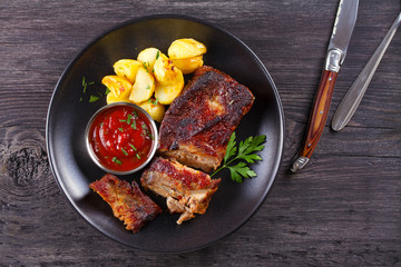 Grilled pork spare ribs with fries on black plate. Roasted sliced barbecue ribs. View from above, top studio shot