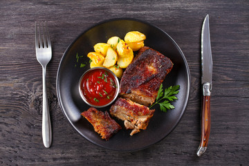 Grilled pork spare ribs with fries on black plate. Roasted sliced barbecue ribs. View from above, top studio shot