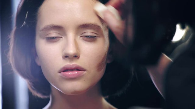 partial view of makeup artist shading contouring on model face with cosmetic sponge