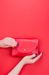 Bright summer fashion ladies accessories. Stylish red leather handbag or clutch bag on a red background. Women hands with bright manicure holding bag. Top View. Flat Lay.