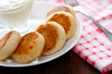 Cheese pancakes with sour cream on a white plate close-up. Can be used for menu design.