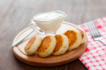 Cheese pancakes with sour cream on a wooden board, with a fork and napkin horizontal format.