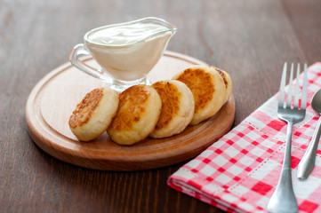 Cheese pancakes with sour cream on a wooden board, with a fork and napkin horizontal format.