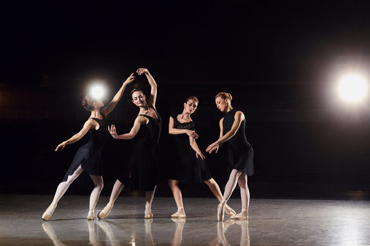 A group of ballerinas are dancing on the scene against a black background.