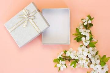 Open empty gift box with ribbon and spring flowers on pink background.