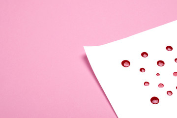 White sheet of paper with red drops of paint on pink background with copy space for text. Trendy and creative backdrop.