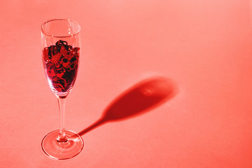 Heart-shaped vibrant red confetti in a champagne glass on coral background with copy space for text. Close-up. Holiday, love and celebration concept.