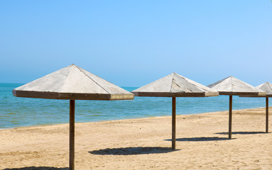 Beautiful empty beach. Sea coast with wooden umbrella and blue sky. The calm sea on a summer day in a tourism and vacation concept. 