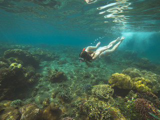 Young woman is swimming among coral reefs in shallow water and looking underwater sealife.