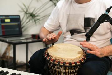 Close up of musician playing djembe drum instrument in home music studio.