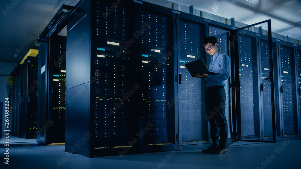 Aufkleber In Data Center: Male IT Technician Running Maintenance Programme on a Laptop, Controls Operational Server Rack Optimal Functioning. Modern High-Tech Telecommunications Operational Super Computer.
