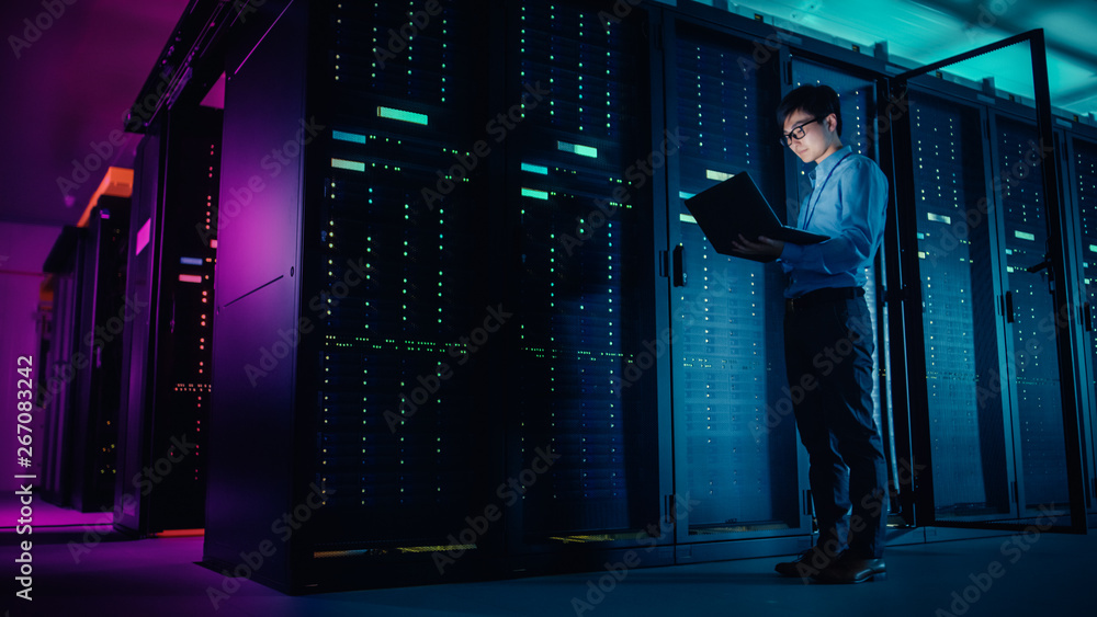 Aufkleber In Data Center: Male IT Technician Running Maintenance Programme on a Laptop, Controls Operational Server Rack Optimal Functioning. Modern High-Tech Operational Super Computer in Neon Colours, Lights