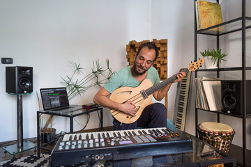Musician playing electric guitar in home music studio.