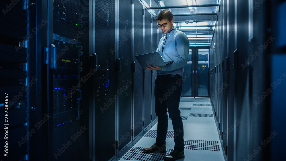 Fototapete In Data Center IT Engineer Stands Before Working Server Rack Doing Routine Maintenance Check and Diagnostics Using Laptop. Concept of Cloud Computing, Artificial Intelligence, Supercomputer