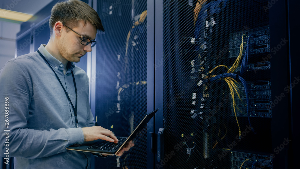 Aufkleber In Data Center IT Engineer Stands Before Working Server Rack Doing Routine Maintenance Check and Diagnostics Using Laptop. Visible Computer Hardware Equipment, Broadband Fiber Optic Cables LED Lights.