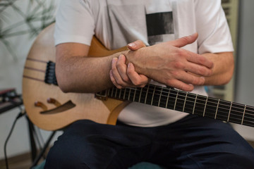 Musician having wrist pain while playing electric guitar in home music studio.