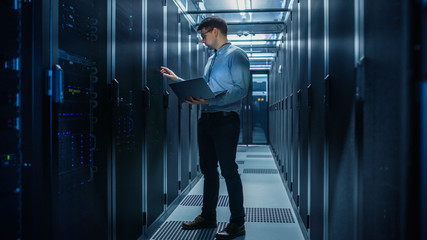 In Data Center IT Engineer Stands Before Working Server Rack Doing Routine Maintenance Check and...