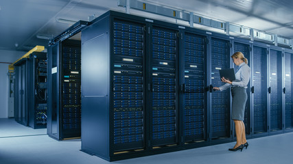In Data Center: Female IT Technician Opens Rack Cabinet and Runs Maintenance Program on Laptop,...