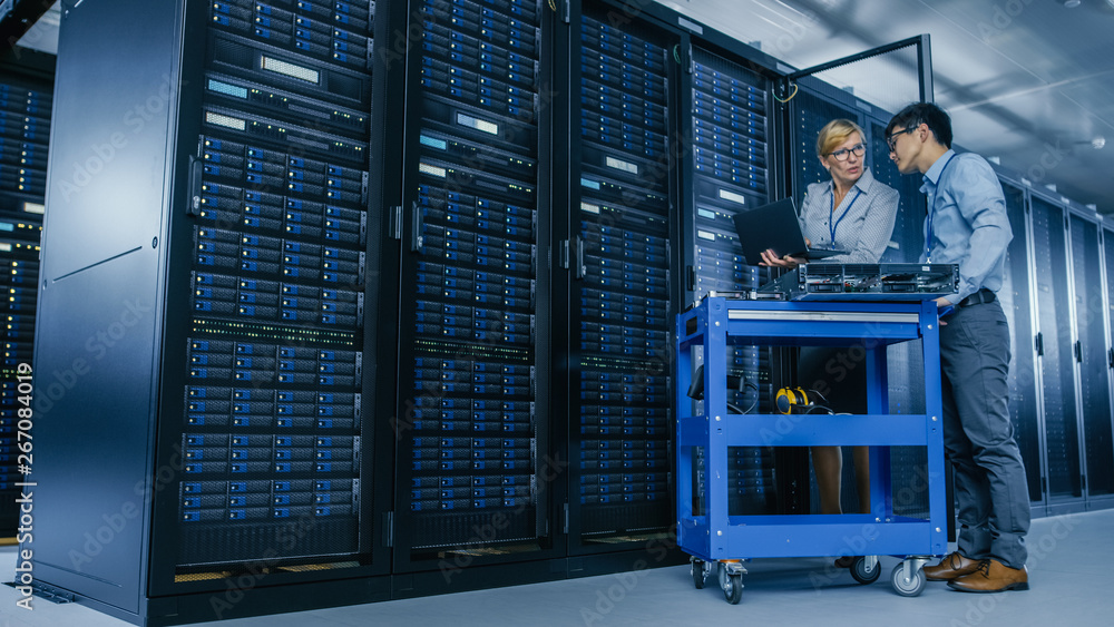 Fototapete In the Modern Data Center: Engineer and IT Specialist Work with Server Racks, on a Pushcart Equipment for Installing New Hardware. Specialists Doing Maintenance and Diagnostics of the Database.