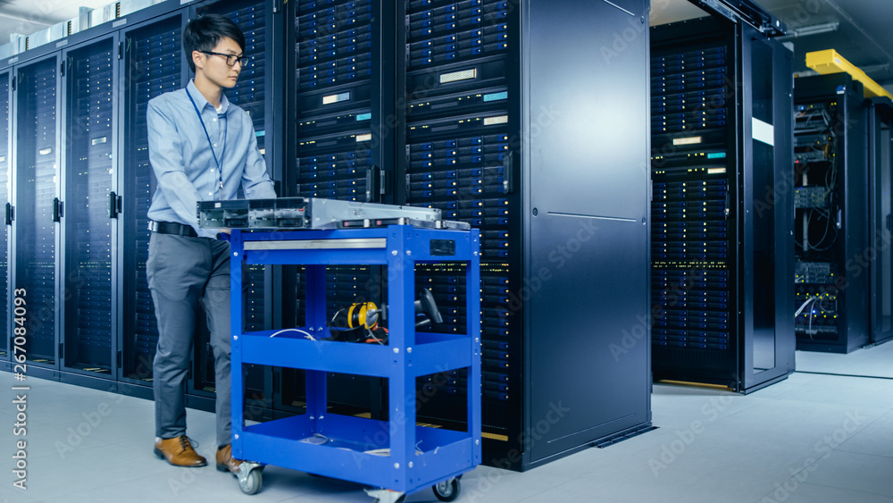 Aufkleber In the Modern Data Center: IT Technician Working with Server Racks, Pushes Cart Between Rows of Server Racks. On a Pushcart New Hardware for System Update. Engineer Doing Maintenance and Diagnostics.