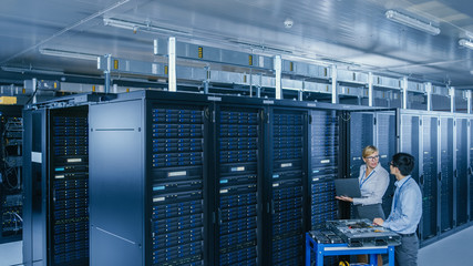 In the Modern Data Center: Engineer and IT Specialist Work with Server Racks, on a Pushcart...