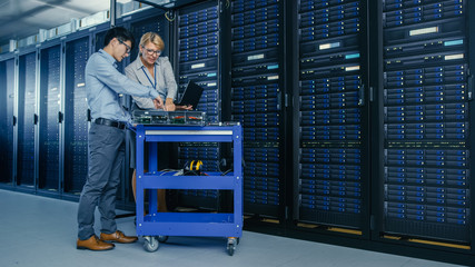 In the Modern Data Center: Engineer and IT Specialist Work with Server Racks, on a Pushcart...