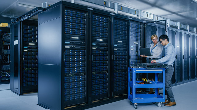 In the Modern Data Center: Engineer and IT Specialist Work with Server Racks, on a Pushcart Equipment for Installing New Hardware. Specialists Doing Maintenance and Diagnostics of the Database.