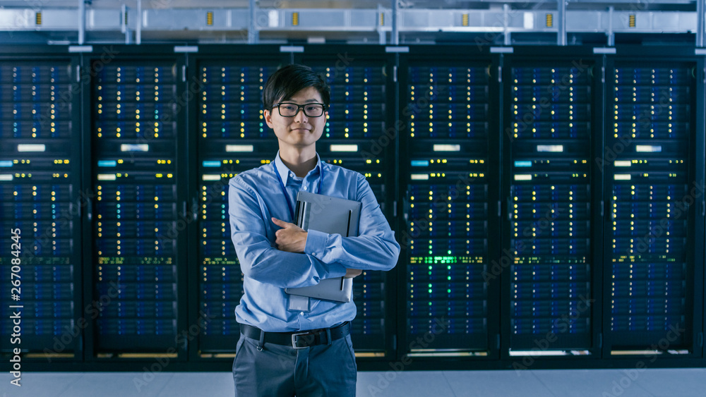 Leinwandbilder  In the Modern Data Center: Portrait of IT Engineer Standing with Server Racks Behind Him, Holding Laptop after Finishing Doing Maintenance and Diagnostics Procedure.