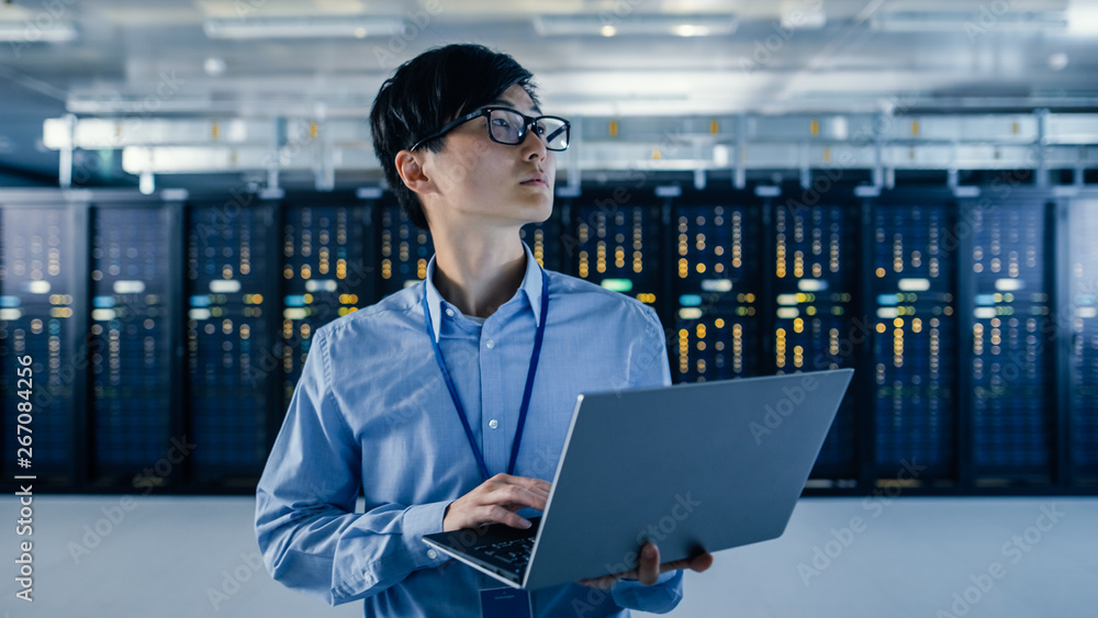 Poster In the Modern Data Center: Portrait of IT Engineer Stand Near Server Racks, Finishing Maintenance and Diagnostics Procedure Holding Laptop.