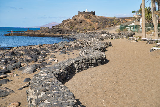 Wall on promenade of Playa grande made of black lava sones leading to the mirador on hill in Puerto del Carmen, Lanzarote, Spain