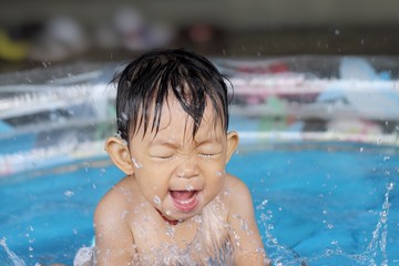 In the summer season, Asian baby child girl take a swimming in a water pool. She happy and smiling.